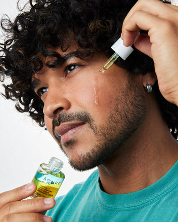 Man applying Radically Rejuvenating Dual Phase Bakuchoil Serum on this face with a glass dropper
