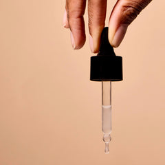 Hand holding a dropper with a beige background