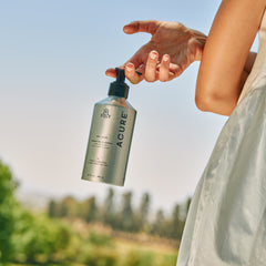Person holding an ACURE Farm collection bottle outdoors with a blurred natural background