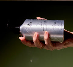 Hand holding a body wash oil bottle with a dark background