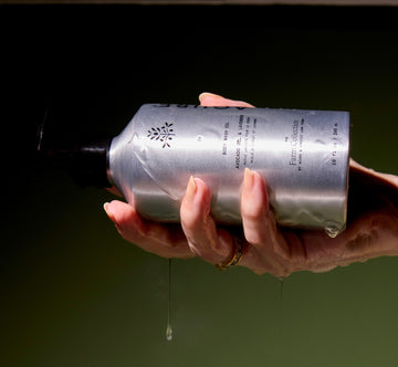 Hand holding a body wash oil bottle with a dark background