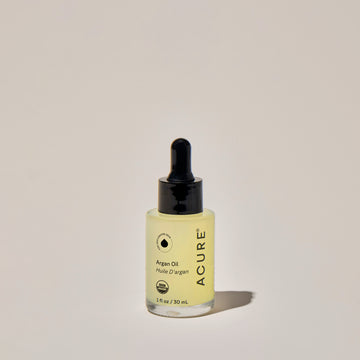 A clear glass bottle with a dropper containing organic 'Argan Oil ', labeled ACURE on a neutral background.