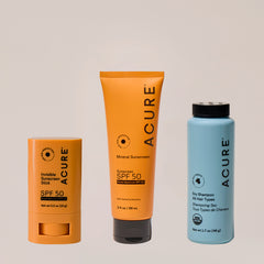 A set of ACURE brand beauty products including a Sun screen stick SPF 50, a Muneral sunscreen SPF 50 tube, and a dry shampoo bottle.