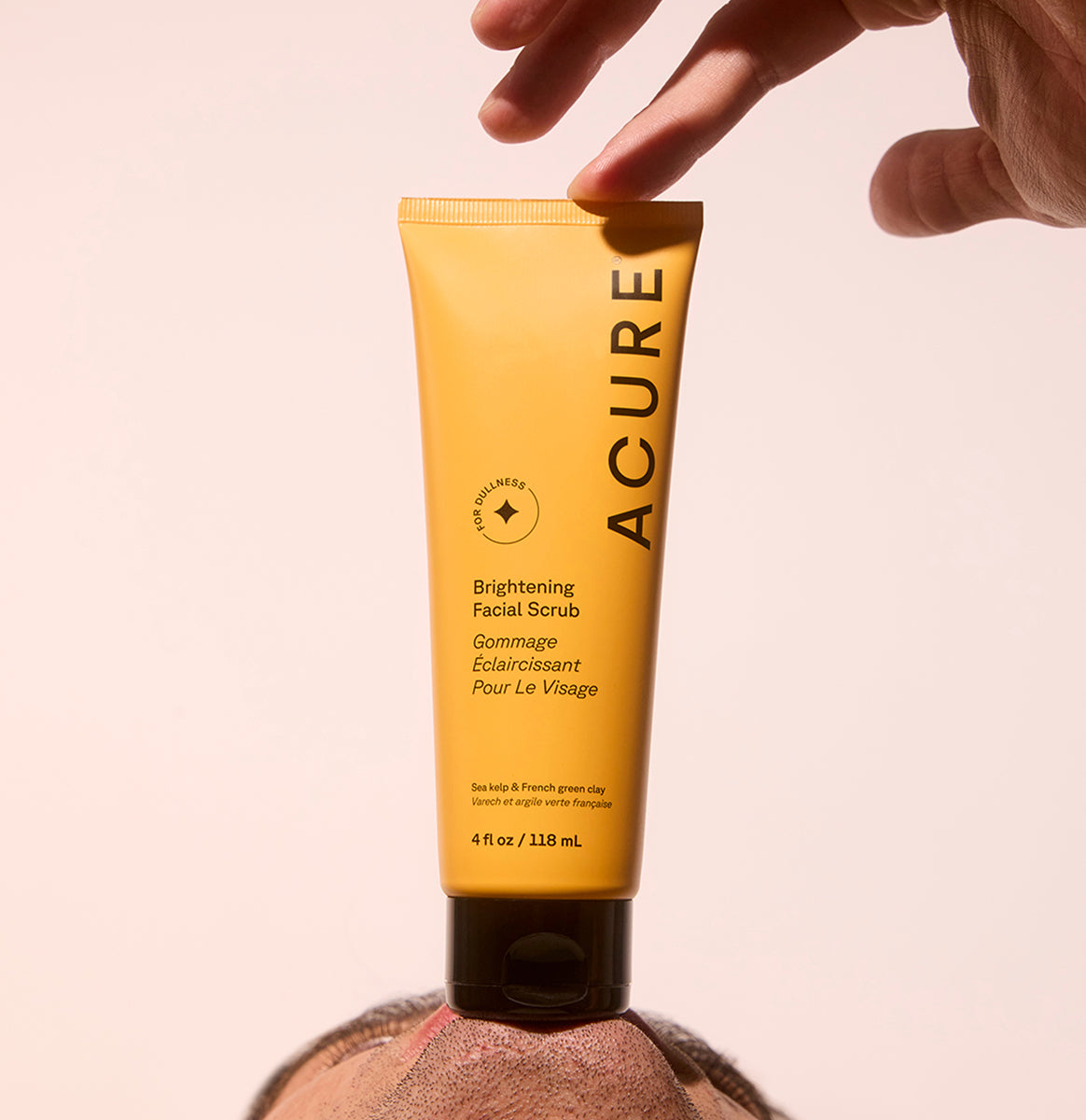 Man holding a tube of Acure Brightening Facial scrub against his chin, holding the top with his hand