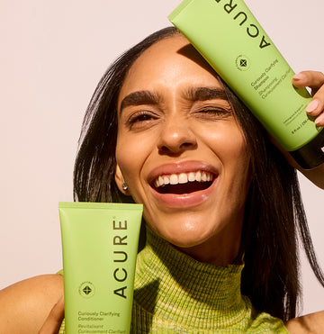 Woman holding Curiously Clarifying Conditioner and shampoo against her face focusing on hair freshness