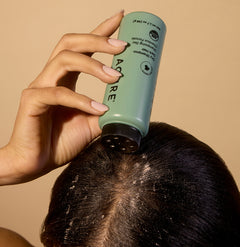 Woman applying dry shampoo directly to her scalp, focusing on hair freshness and quick styling