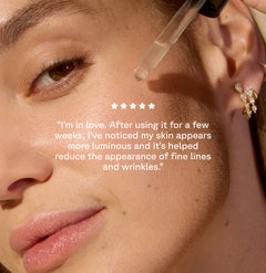 Woman applying Serum with a dropper on her cheek on the background with text on top: A customer review: "I'm in love. After using it fot a few weeks, I've noticed my skin appears more luminous and it's helped reduce the appearance of fine lines and wrinkles"
