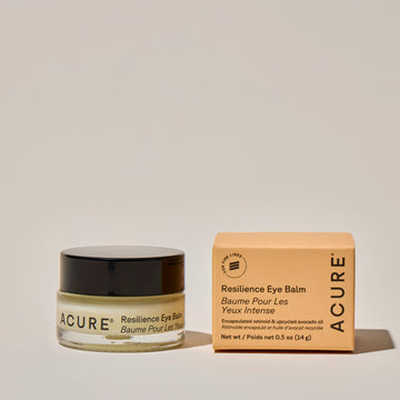 Glass Jar of Acure Resilience Eye Balm next to the box packaging on a neutral background