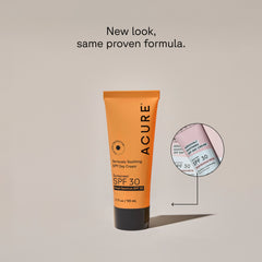 A yellow tube of ACURE Seriously Soothing SPF Day Cream with SPF 30 protection on a neutral bcakground with a circle displaying the old packaging and a text calling out: NEw look, same proven formula