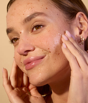 Woman applying skincare product to her face with a beige background