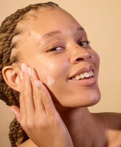 Woman applying cream to her face with a beige background