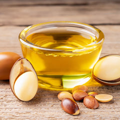 Argan oil in a glass bowl with seeds all displayed on top of a wooden board