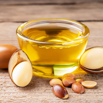 Argan oil in a glass bowl with seeds all displayed on top of a wooden board