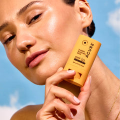 Woman holding Acure sunscreen stick against a blue sky background