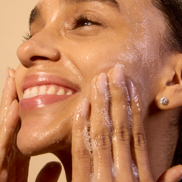 Woman applying acure's cleanser to her face