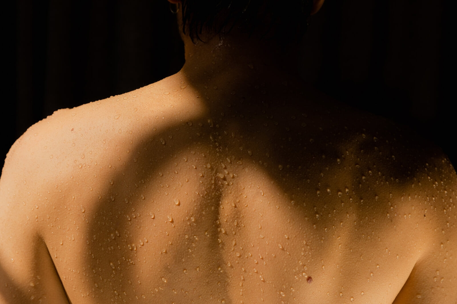 Person's back with glistening water droplets, as if freshly out of a bath, evoking refreshed and hydrated skin.