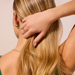 Close-up of a person adjusting their blonde hair with a hand on a plain background