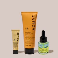 A set of three ACURE skincare products, including a tube of facial cleanser, a bottle of facial serum, and a tube of Facial  mosturizer against a neutral background.
