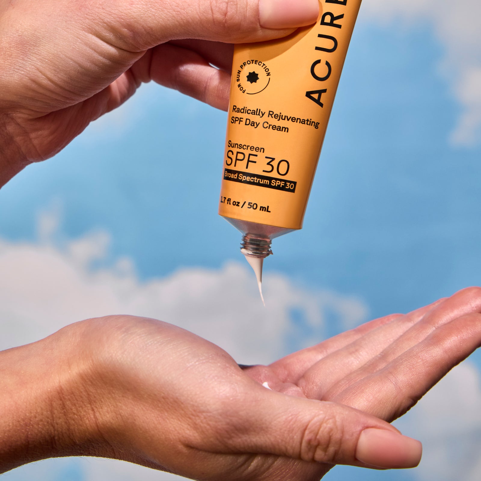 Woman applying cream on her hand with a blue sky background