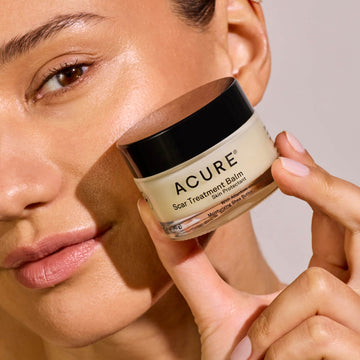 Person holding a jar of Acure Scar Treatment Balm close to their face.