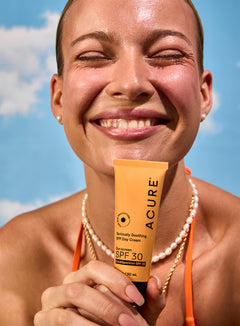 Woman holding Acure sunscreen – clean, reef-safe sun protection with a radiant finish