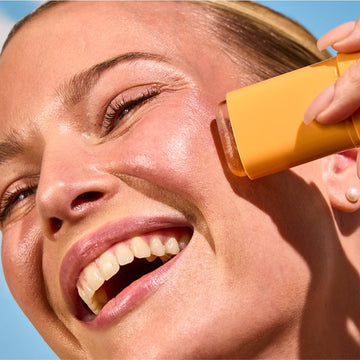 Woman applying Acure Invisible Sunscreen Stick directly to her cheek, demonstrating smooth, mess-free application.