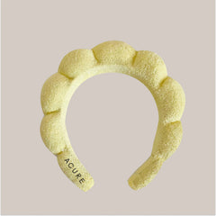 Yellow textured headband with 'Acure' branding on a light pink background