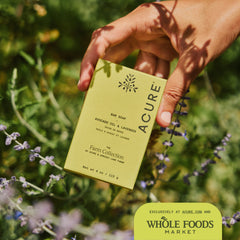Hand holdingAvocado oil and lavender Acure x Apricot Lane Farm  soap bar in front of lavender plants