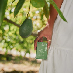 Person holding a box of Acure bar soap  with an avocado on a tree in the background