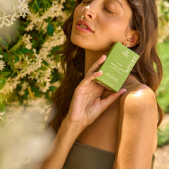 Woman holding a vegan, non-toxic bar soap  box outdoors with plants in the background