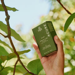 Hand holding a green Acure box among leaves