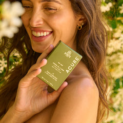 Woman holdin Acure x Apricot Lane Farm bar soap made with regenrative avocado oil  in a natural setting with flowers.