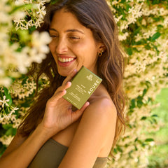 Woman holding a green Acure Farm Collection box product against a floral background