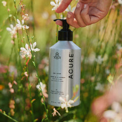 Acure Farm Collection lotion bottle held by a hand with flowers in the background