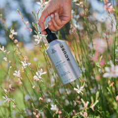 Hand holding a bottle of 'ACURE' farm collection lotion among flowers