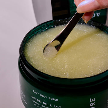 Jar of salt body scrub with a spoon scooping out some of the scrub.