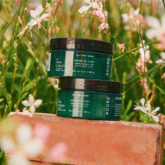 Two Acure skincare products on a wooden block with flowers in the background