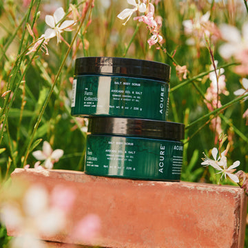 Two Acure skincare products on a wooden block with flowers in the background
