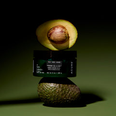 Avocado body scrub jar with half an avocado on a dark green background