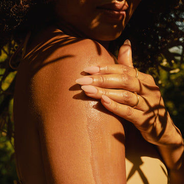 Hand applying lotion to a shoulder with a natural background