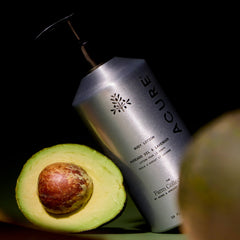 Acure body wash oiol with an avocado on a dark background