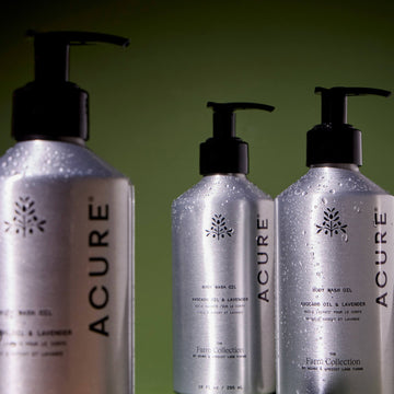 Three bottles of Acure body wash oil on a green background