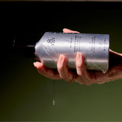 Hand holding a silver bottle with a dark background
