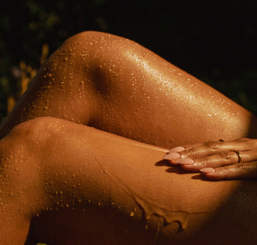 Woman applying avocado body-wash oil on skin against a dark background
