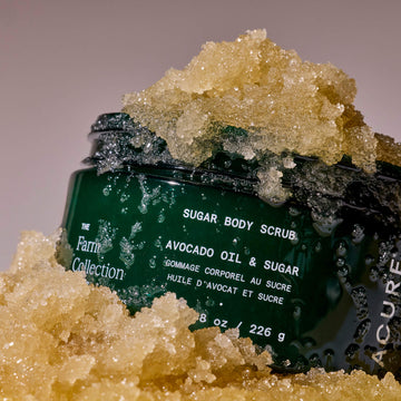 Green jar of sugar body scrub with avocado oil and sugar on a gray background