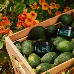 Wooden crate filled with avocados and jars surrounded by greenery and flowers