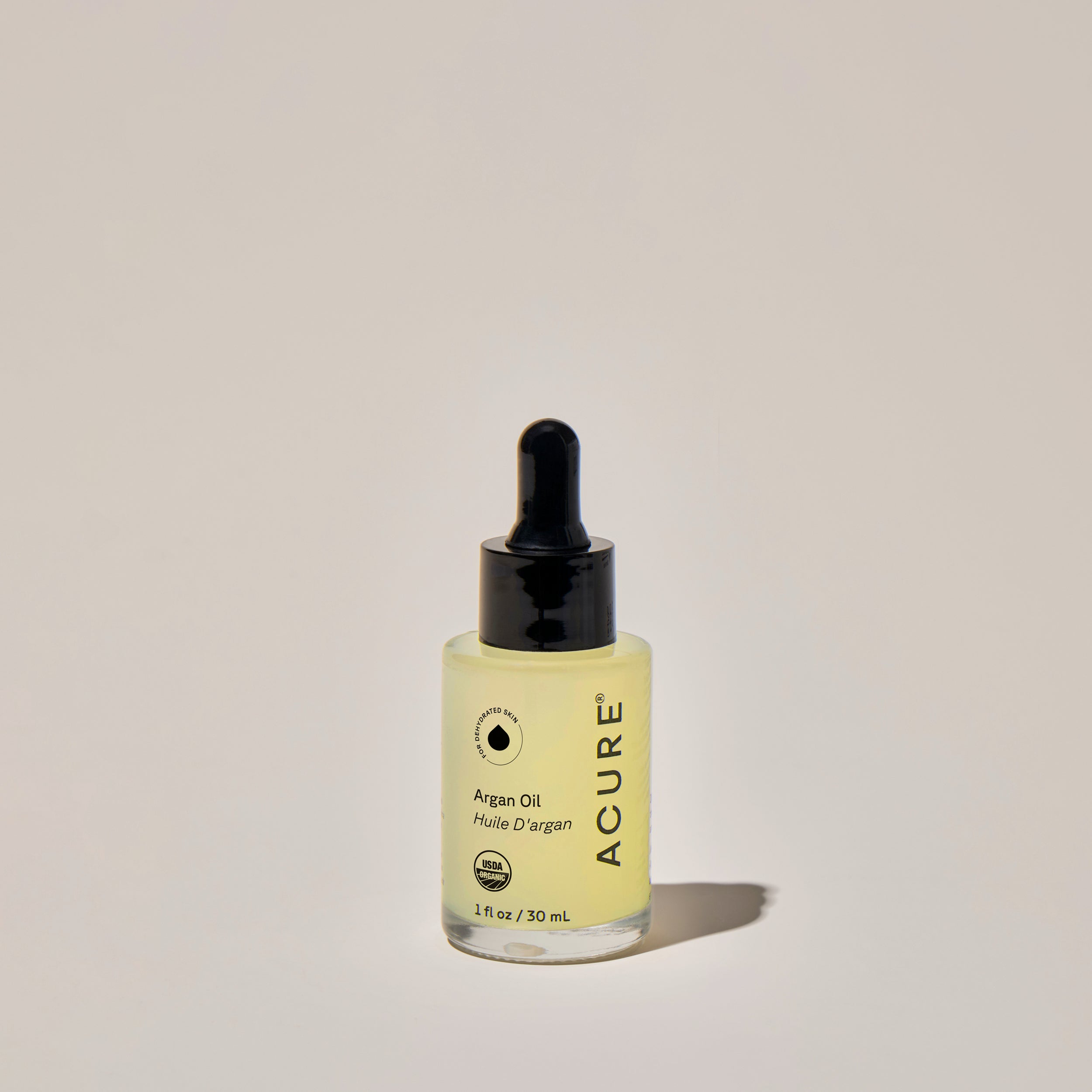 A clear glass bottle with a dropper containing organic 'Argan Oil ', labeled ACURE on a neutral background.