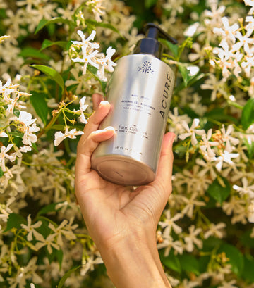 Hand holding a silver bottle labeled 'Acure' against a floral background