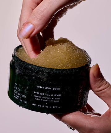 Person holding a container of sugar body scrub with visible branding.
