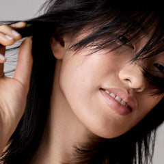 Close-up of a woman with dark hair touching her face against a neutral background